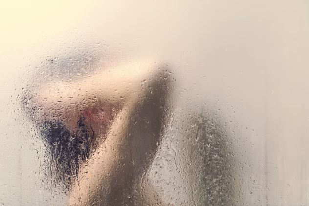 Moteris po dušu už stiklo su vandens lašais