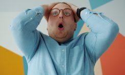 Man with glasses grabs head in shock