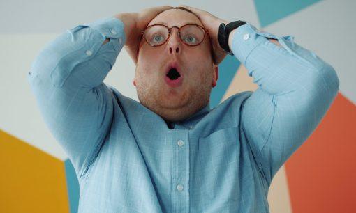 Man with glasses grabs head in shock