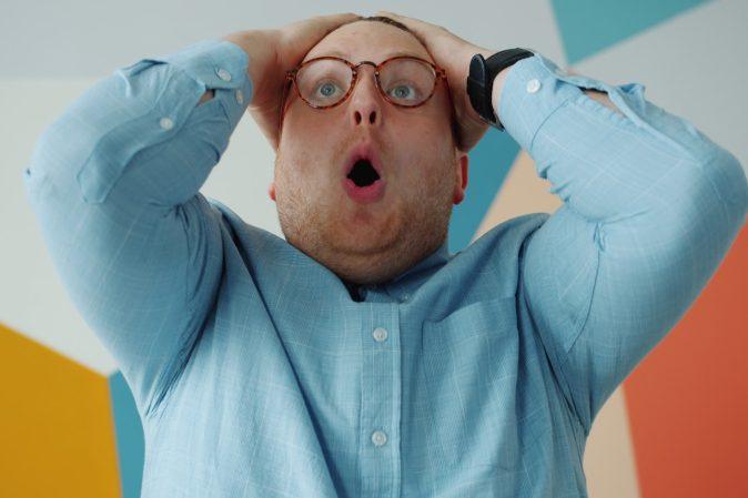 Man with glasses grabs head in shock
