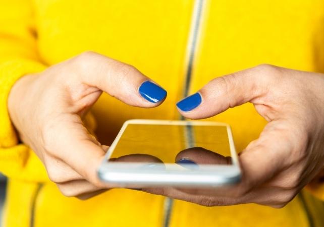 Asmuo geltonoje striukėje laiko telefoną