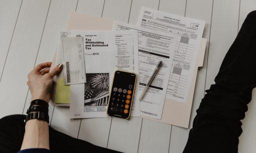 person holding paper near pen and calculator