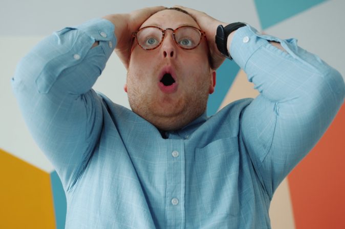 Man with glasses grabs head in shock